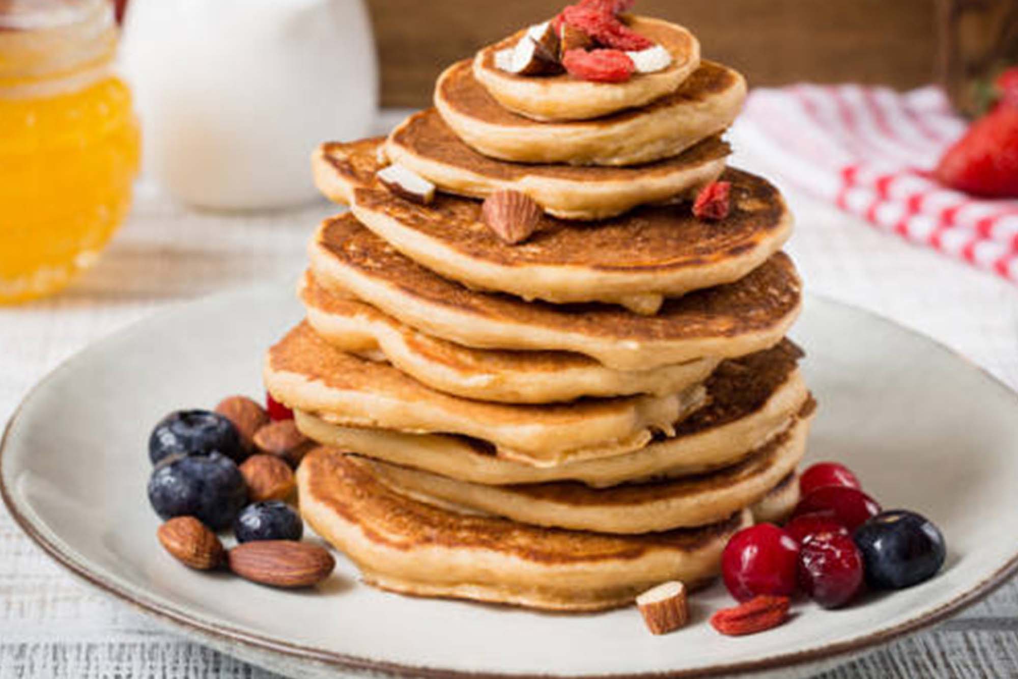 picture of a large stack of pancakes with nuts and berries around and on top.